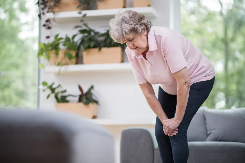 senior woman grips knee with indoor plant display 2026 03 10 03 56 41 utc