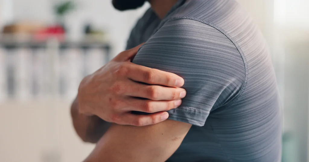 man massaging aching shoulder in bright room 2026 03 25 03 46 04 utc