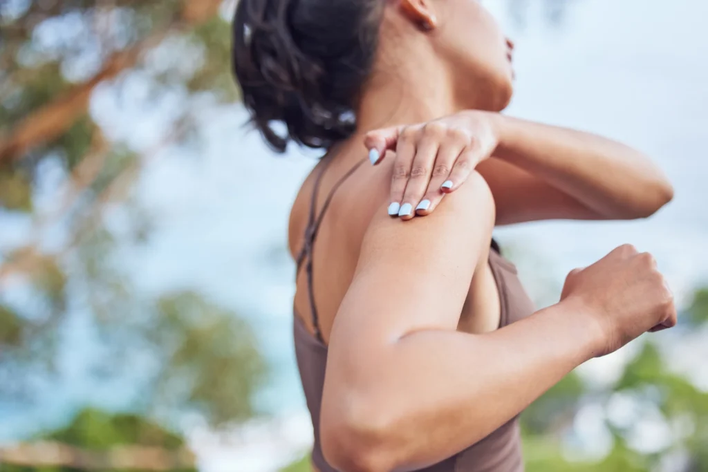 woman massaging shoulder outside in green setting 2026 03 25 07 39 46 utc